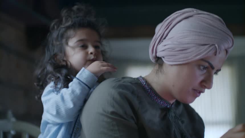 A mother and daughter use a tablet in bed