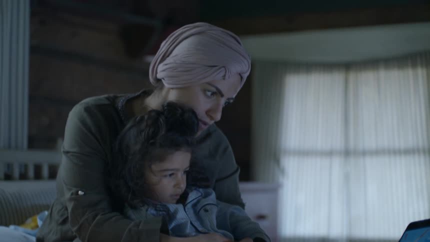 A woman and child watch a tablet in bed