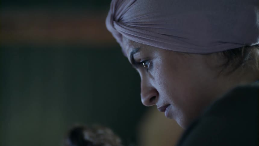 A woman wearing a headdress sits and stares intensely
