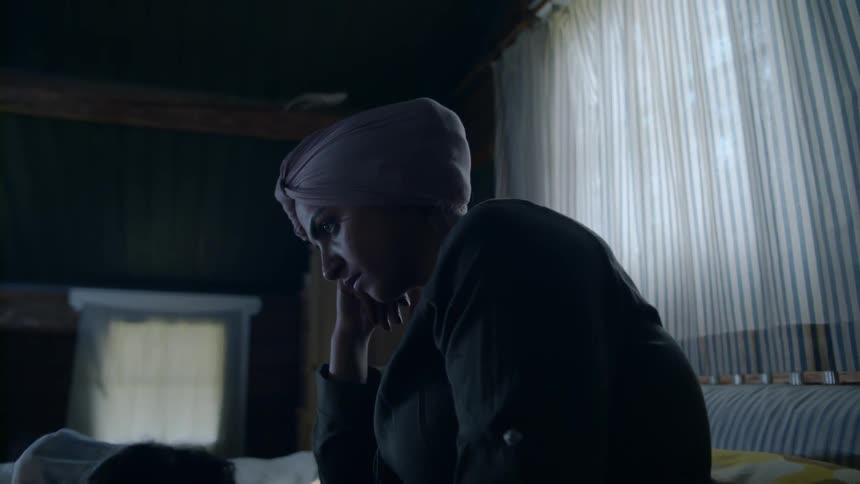 Woman wearing a head wrap watching something on a tablet with a girl laying in her lap