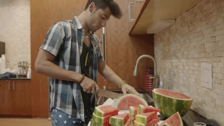 Man carefully slices watermelon by the sink