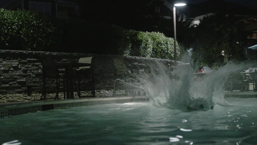 A man front flips into a pool at night