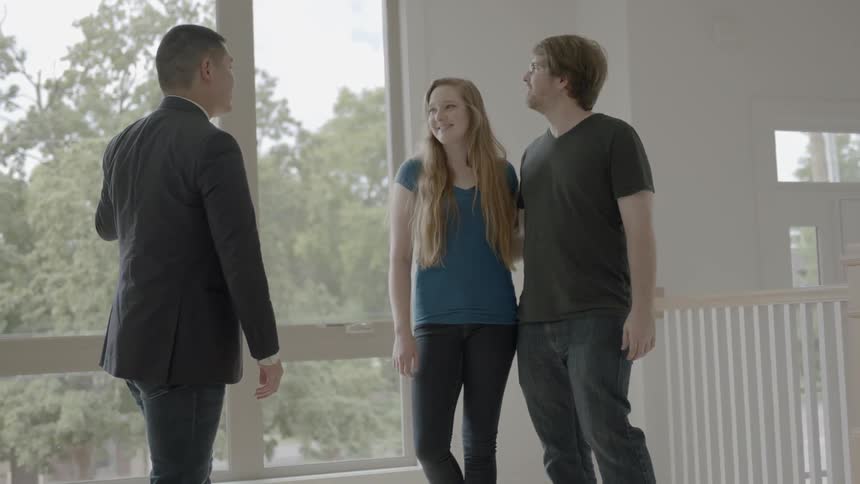 Man wearing suit shows woman and man house in front of window