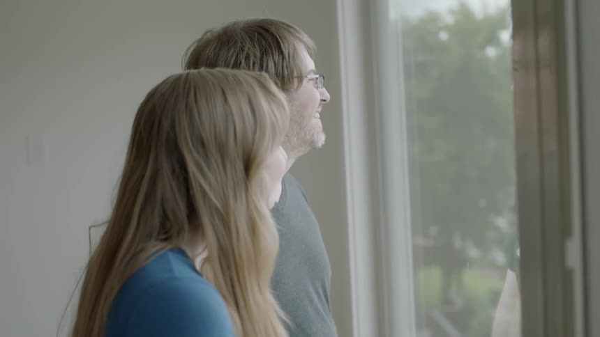 A man and woman look outside a window