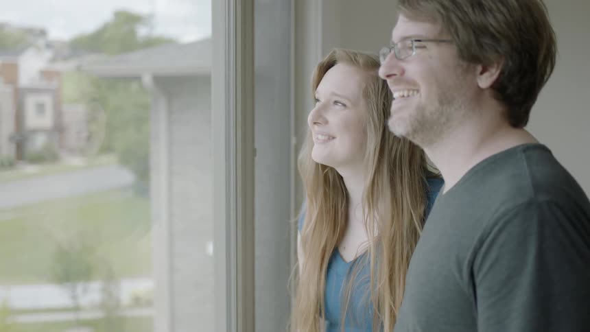 A man and woman smiles as they look out the window at the neighborhood