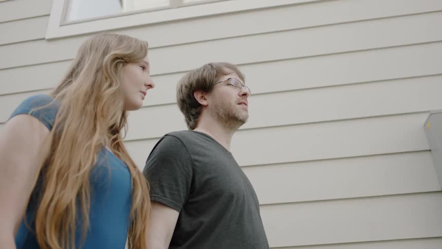 A young couple stand next to a wooden clad building and nod
