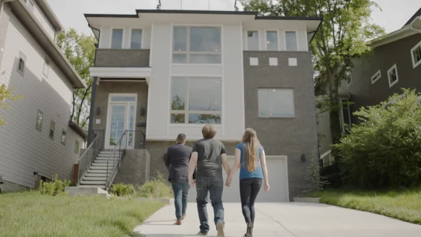 Three people are walking towards a house