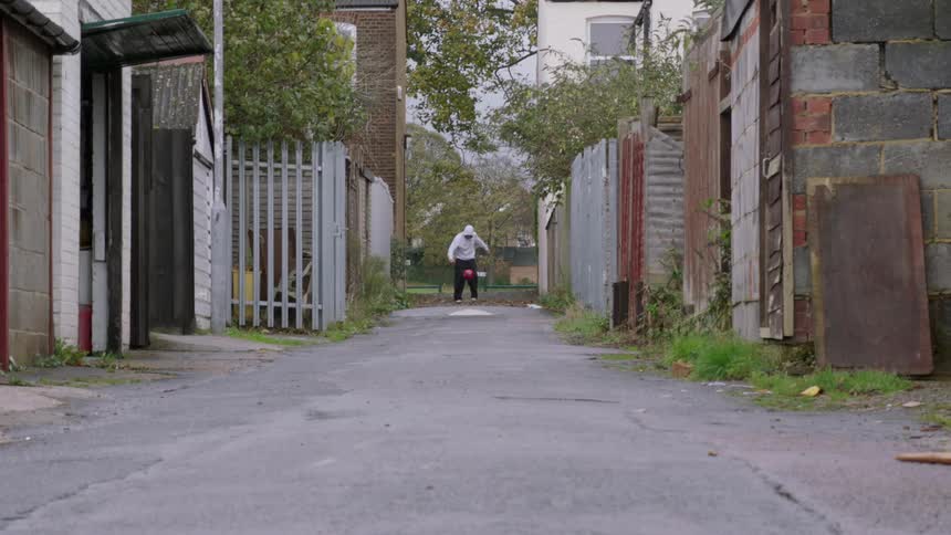 A man balancing and kicking a ball in an alley