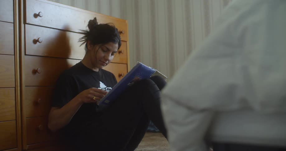 A woman sits up against a dresser looking at photos