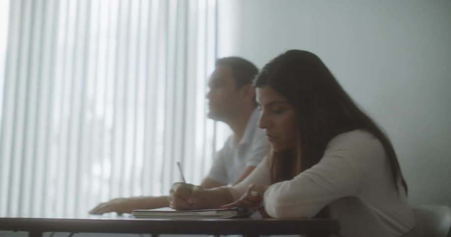 An adult student takes notes as a teacher speaks