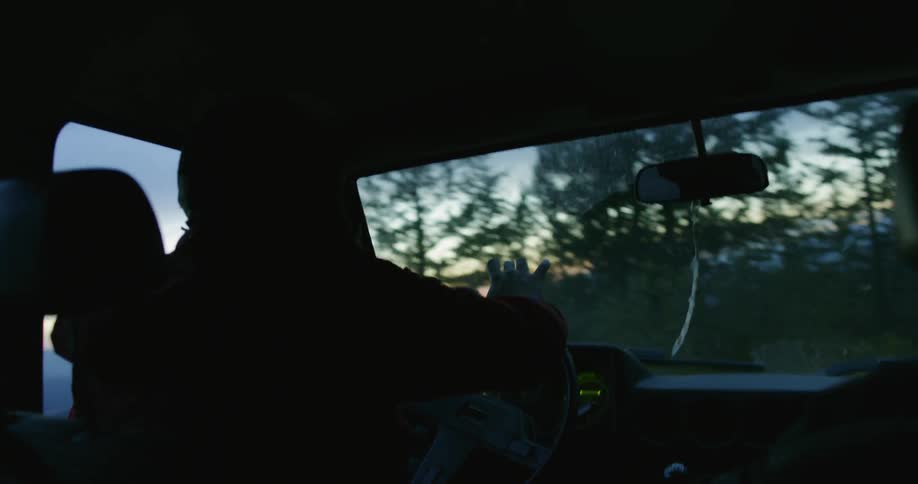 A man drives a car in a mountain forest at sunset