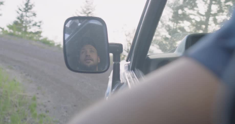 Man wearing cap leaving his hand outside the car and driving up hill
