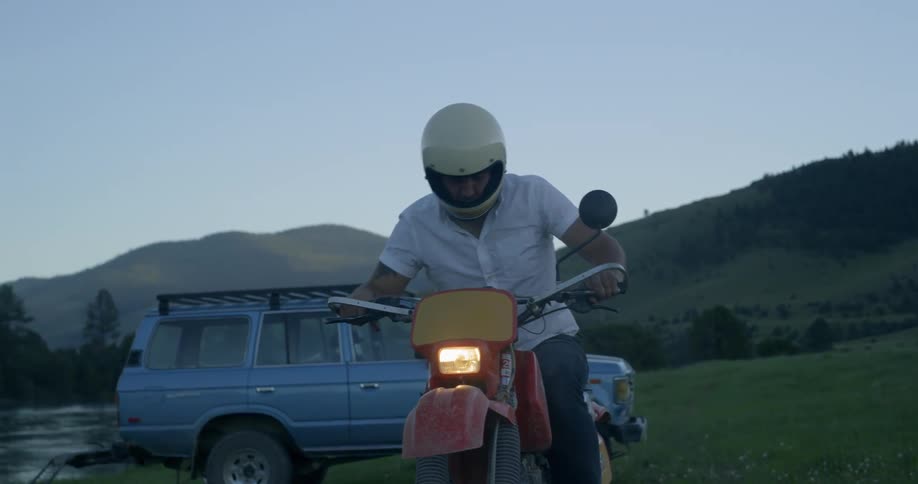 Man starts the bike and moves away in valley at dusk