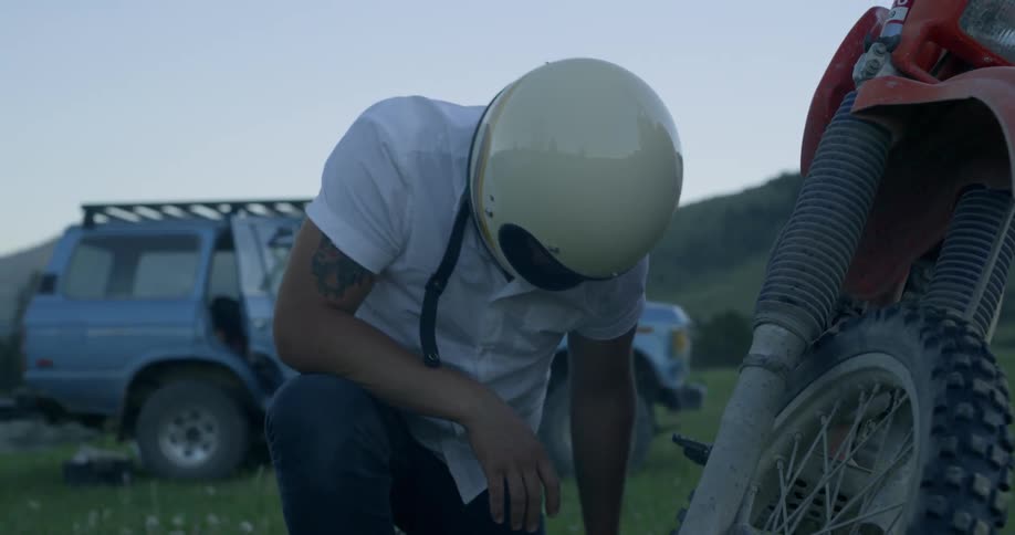 A man kneeling in the grass working on a motorcycle