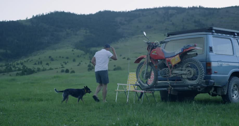 A man and dog walk next to a parked suv in a rural field