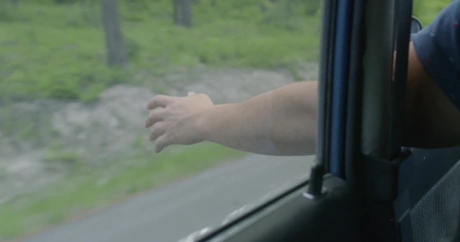 A man is driving with his arm hanging out of the window