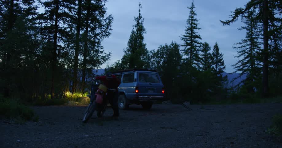 Person walks a motorcycle away from a jeep in the woods