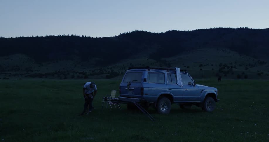 A man puts on pants in an isolated area behind his vehicle