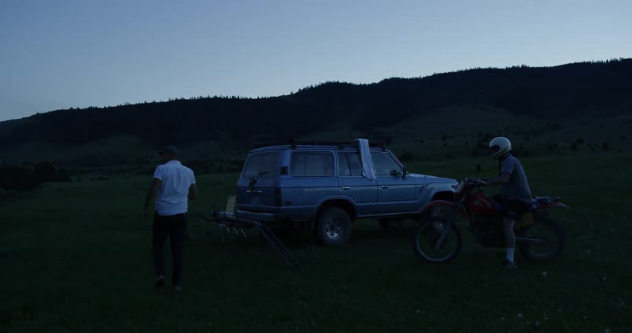 Two men and a dog are near the lake at sunset