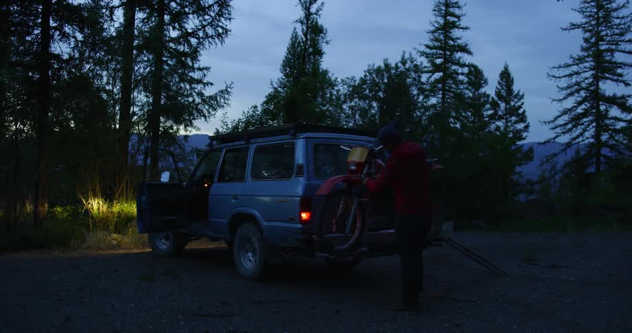 Man puts bike on bike rack in forest at dusk