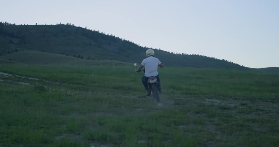 A man wearing a helmet riding a dirt bike through a hilly field