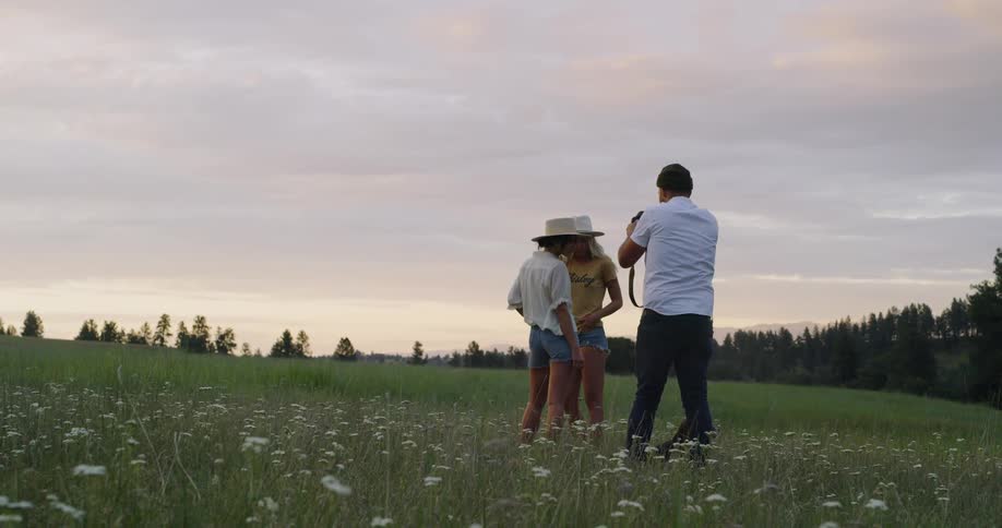 A man takes photographs of two women in the field