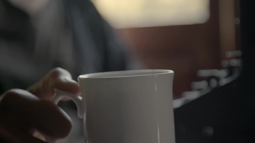 A man setting a coffee mug down on a desk next to a typewriter