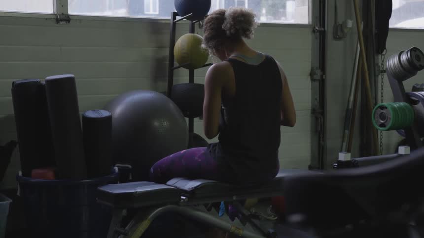 Woman sits on workout bench in gym and wraps hands