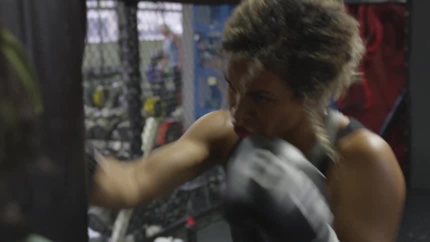 Woman boxer rapidly punches punching bag in gym