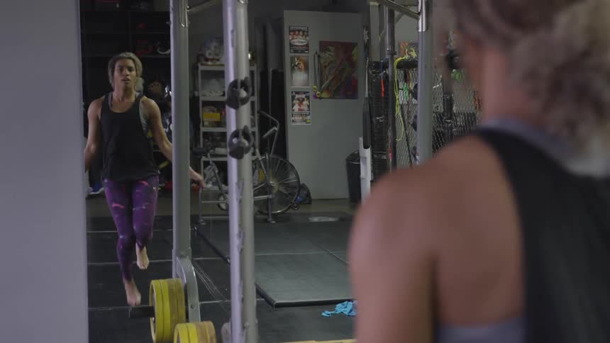 Woman jumps rope barefoot in gym while looking into mirror