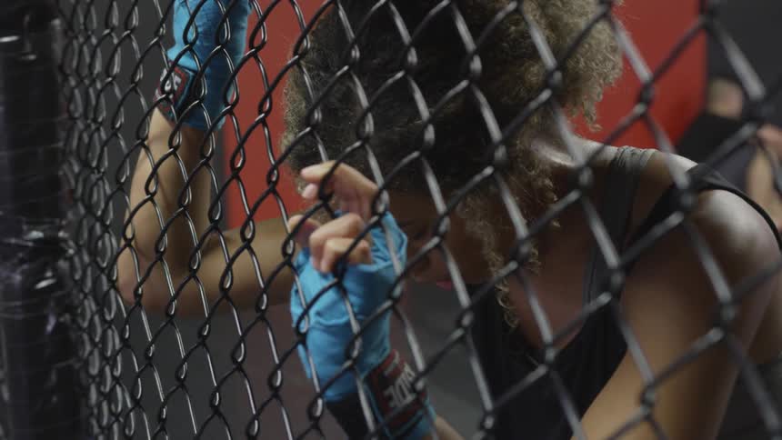 A woman wearing fingerless gloves breathes deeply as she leans against a fence