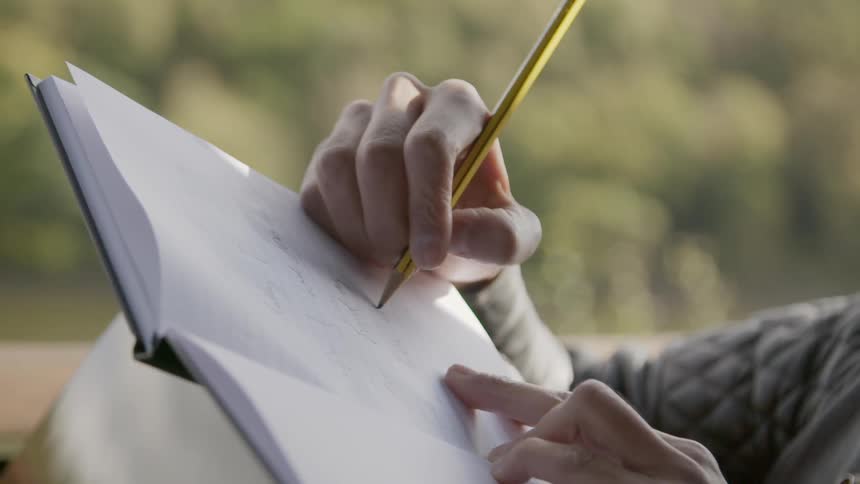 A person writing in a notebook with a pencil