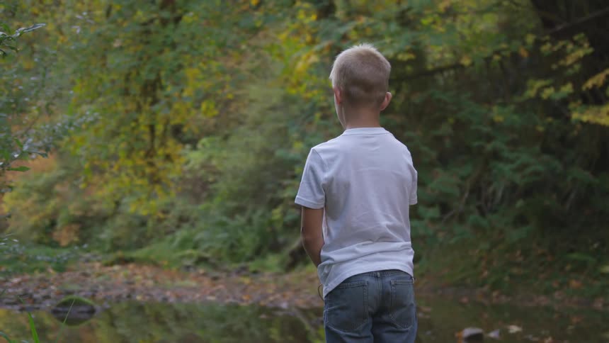 A little boy stands and stares as he holds his fishing rod in the water
