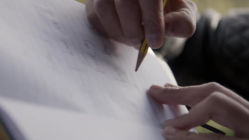 Person writing on paper with a pencil
