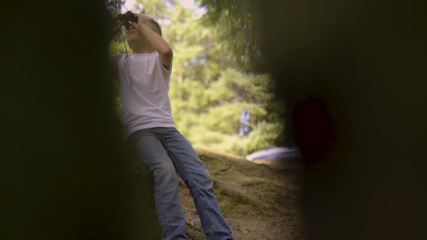 Young boy looks through binoculars in forest