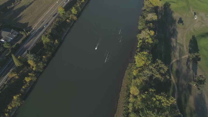 Three rowing boats row in a man made river next to a highway