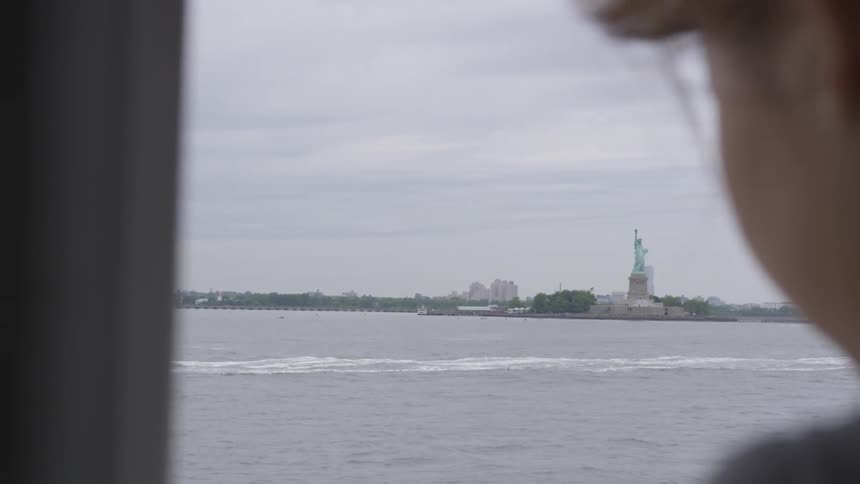 A woman rides a ferry near the statue of liberty