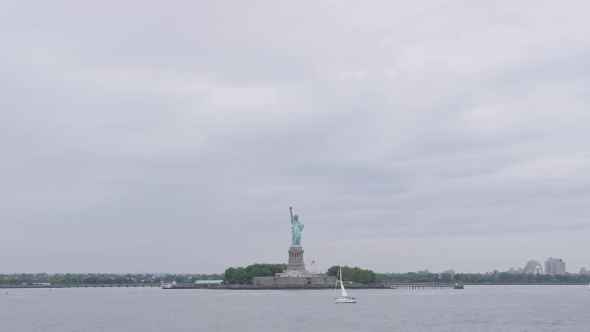 Boats sail near the statue of liberty on a cloudy day
