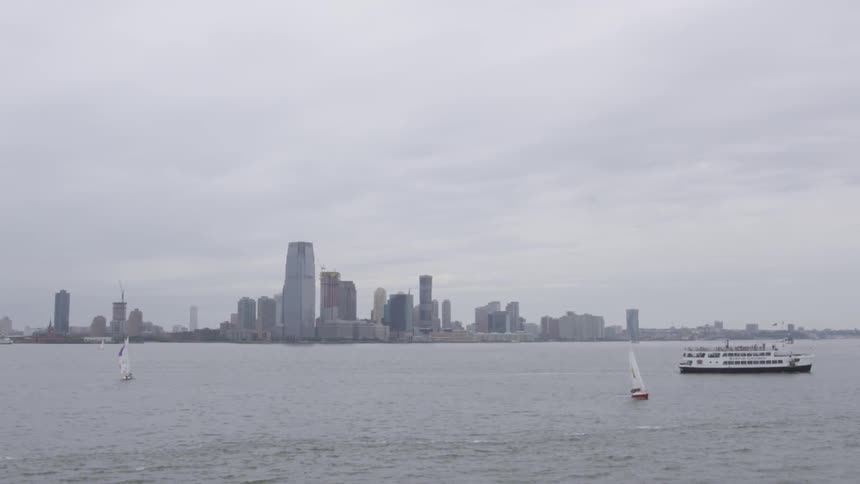Two sailboats and a small cruise ship are on a lake with a city skyline in the background