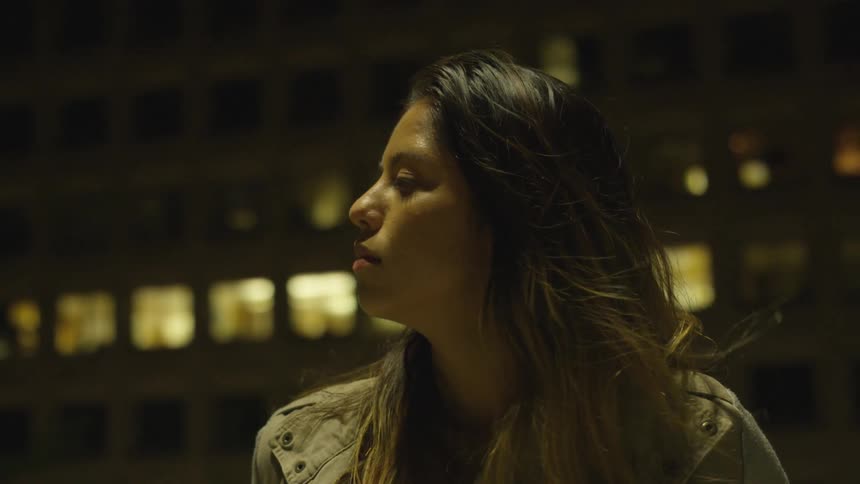 Woman looks at specific direction and thinks in front of building by night