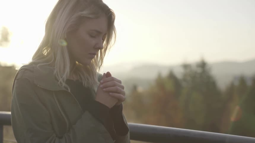 A woman is praying on a hill at sunset