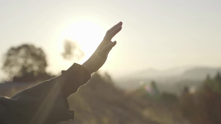 A person reaches their hand up to the sky