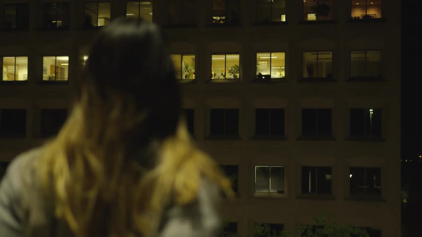 A woman looks up at the building at night