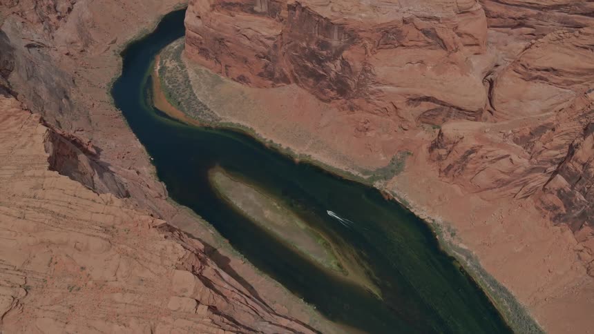 An object moves through the surface of a water source which passes through an otherwise arid desert landscape