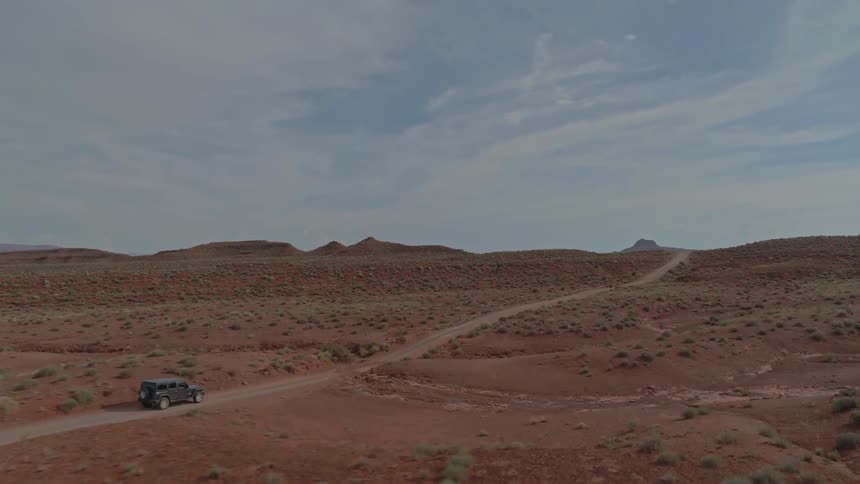 Jeep drives on dirt road through desert in daytime