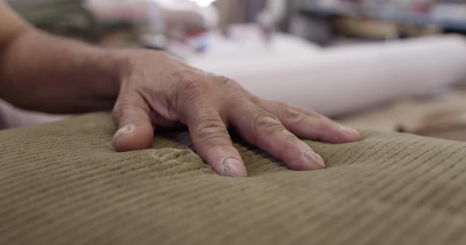A man poking a large needle through a cushion