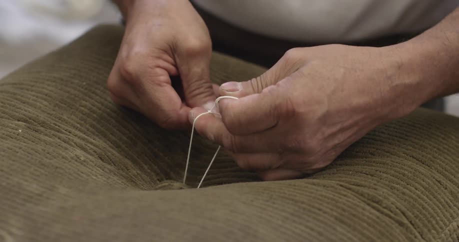 Person sews a button back onto a pillow