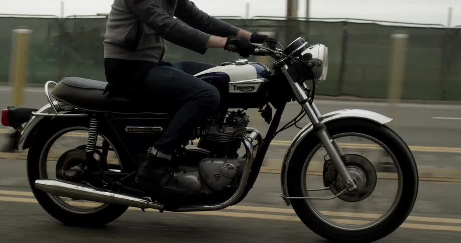 A person rides a motorcycle on a two-way roadway with the ocean in the background