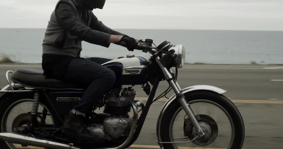 Person riding a motorcycle across a road on a cloudy day
