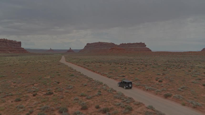 An suv travels on a dirt road in a desert on a cloudy day